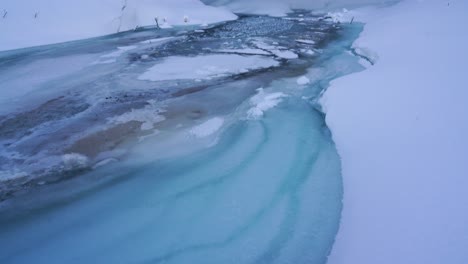 Toma-Aérea-Inclinada-Hacia-Arriba-De-La-Impresionante-Cascada-De-Seljalandsfoss-Que-Se-Estrella-Contra-Un-Río-Helado-Y-Nevado-En-Islandia