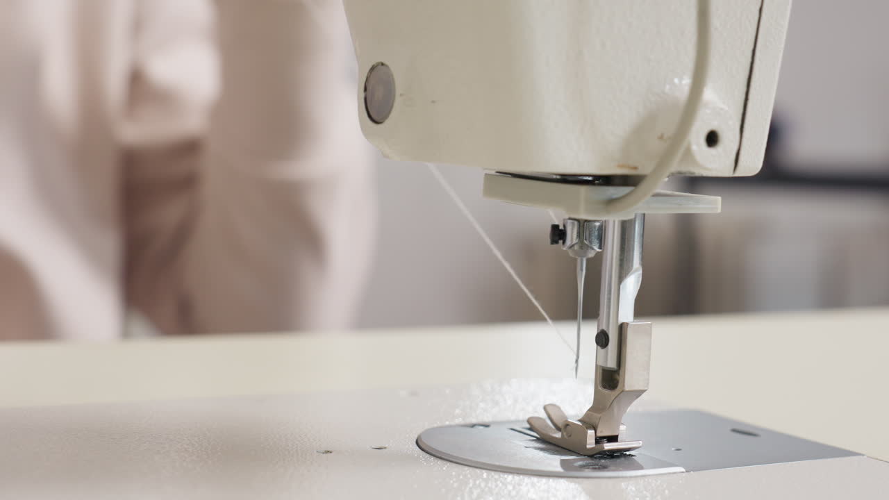 Tailor pulling out thread from needle on sewing machine, emphasizing manual skill, tension management, close view, gentle motion, highlighting bright workspace, and careful approach