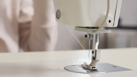 tailor pulling out thread from needle on sewing machine, emphasizing manual skill, tension management, close view, gentle motion, highlighting bright workspace, and careful approach