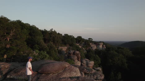 Aerial-drone,-man-standing-on-edge-of-cliff-rise-over-Garden-of-the-Gods,-Southern-Illinois