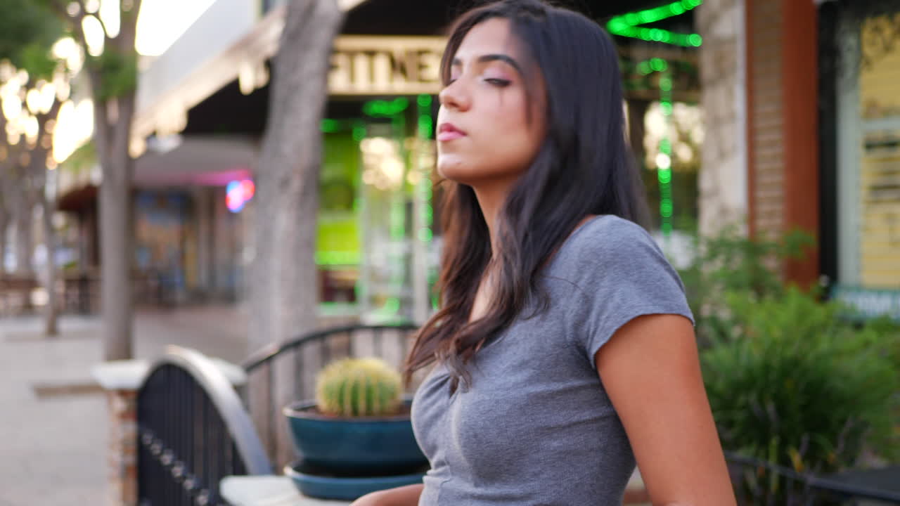 una hermosa mujer hispana de pie y posando en la calle de la ciudad urbana llena de tiendas y tiendas minoristas a cámara lenta