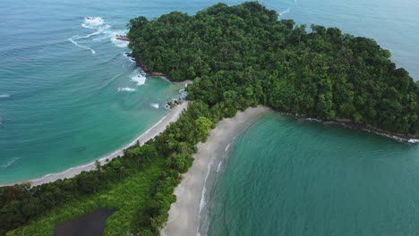 high angle drone lowering shot of waves rooling at both sides of manuel antionio beach