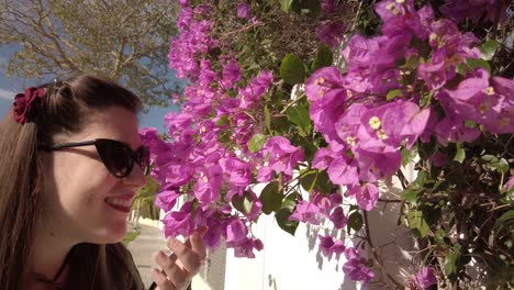 Stylish-woman-with-sunglasses-smells-bougainvillea-flowers-and-smiles,-Slowmo