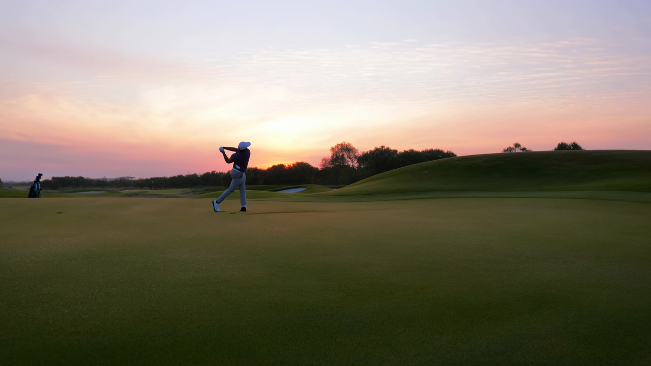 Golfista maschio che esegue lo swing con la mazza da golf su un campo da golf al tramonto, mostrando un'atmosfera rilassata e concentrata. La vista laterale cattura l'erba e il cielo, enfatizzando i vivaci colori verde e blu.