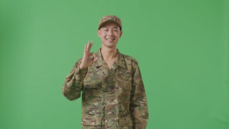 asian man soldier smiling and showing okay gesture to camera while standing in the green screen background studio