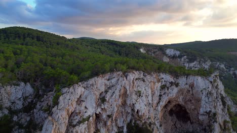 Hikers-rest-on-a-rocky-cliff-among-trees-with-a-view-of-the-green-landscape-during-sunset-in-ibiza