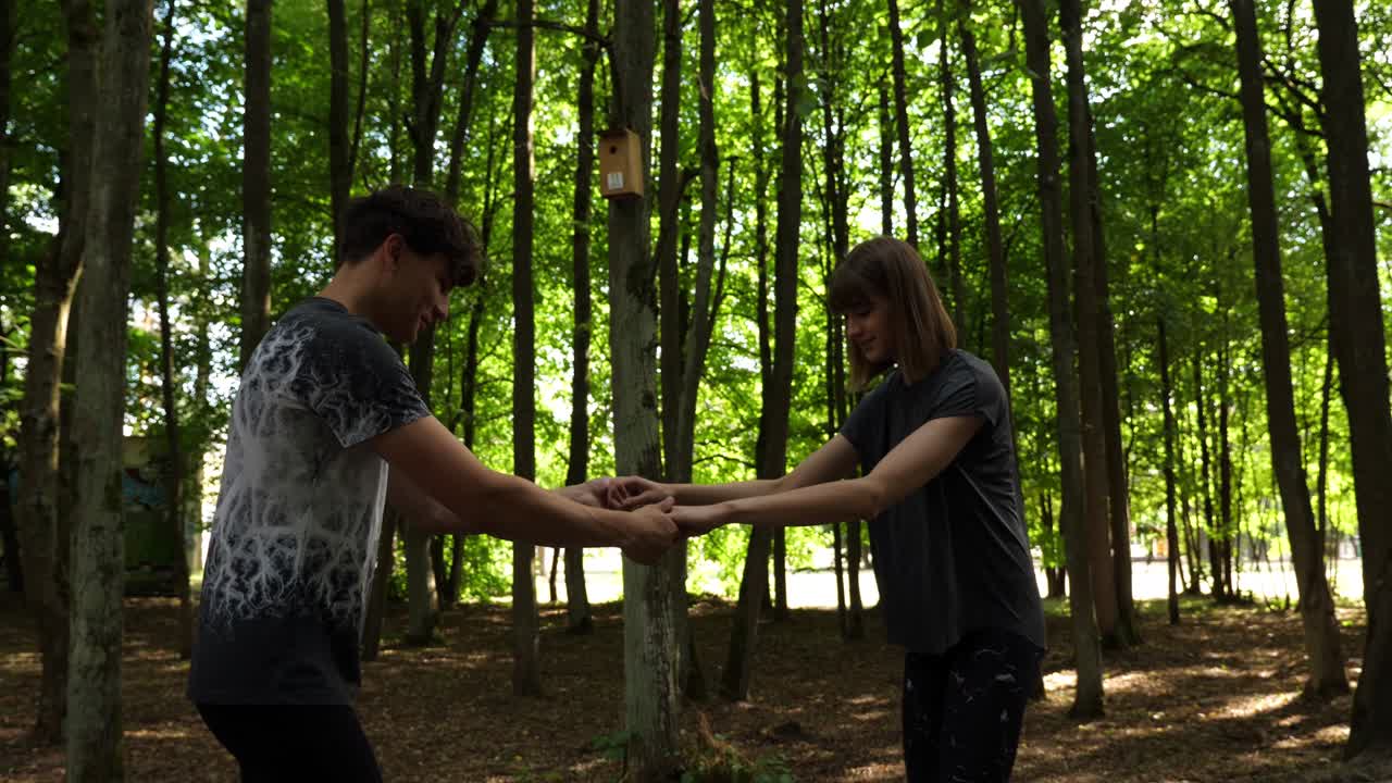 молодая пара учится кататься на роликах в парке, держась за руки, в замедленном движении, на расстоянии,