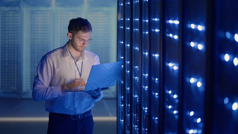 male server engineer in data center. it engineer inspecting a secure server cabinet using modern technology laptop coworking in data center.