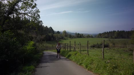 Hiking-man-tightens-backpack-strap-walking-by-field-forest-countryside