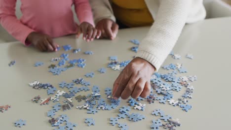 Hands-of-african-american-granddaughter-and-grandmother-doing-jigsaw-puzzle-at-home,-copy-space