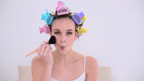 young model in hair rollers putting make up on her face