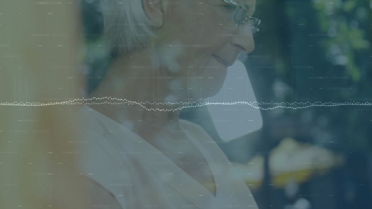 Senior woman receiving tech call on smartphone while writing on tablet with stylus and waveform