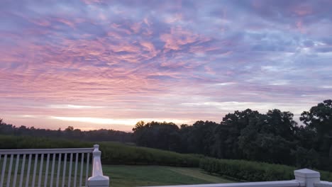 Colorful-sunrise-timelapse,-beautiful-clouds-moving-across-sky-revealing-pink,-orange,-red,-hues,-rural-countryside-setting-on-a-peaceful-deck-overlooking-hillside-orchard,-time-lapse,-hyperlapse