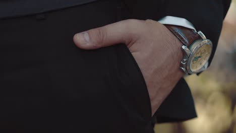 joven empresario pone la mano en el bolsillo de sus pantalones tiene un reloj en la mano un close-up cámara lenta