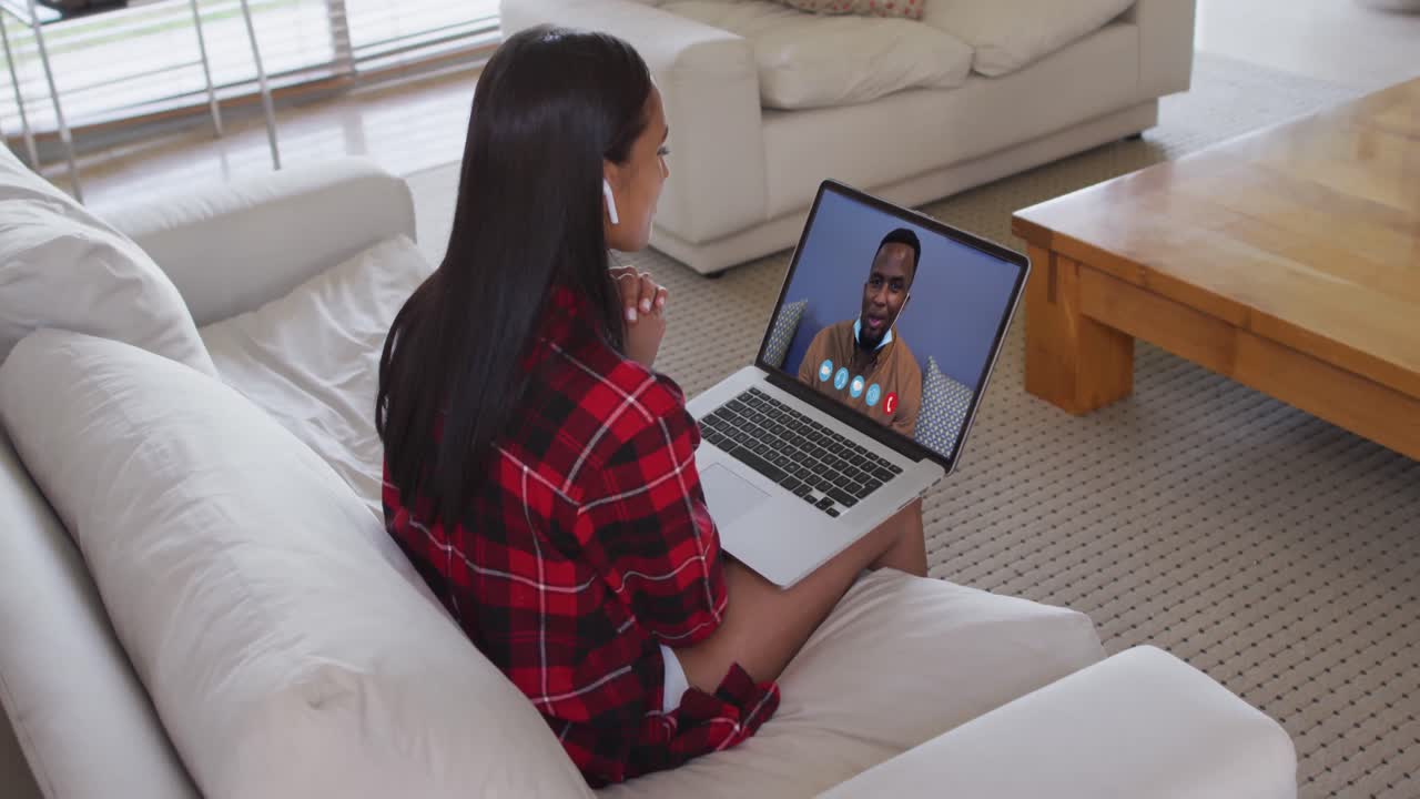 Mixed race woman on laptop video chat using wireless earphones at home