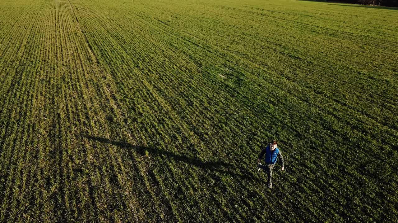Boy running on the green field towards the moving camera and looking into it. One active kid going fast in the rural place outdoors to the other little boy. Aerial view