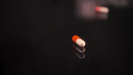 Pills-falling-down-on-a-black-glass-surface,-mirror-surface-with-a-reflection-on-black-background