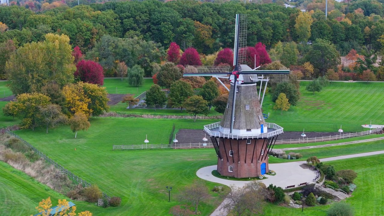 Kincir angin Belanda dikelilingi rumput hijau dan pepohonan musim gugur berwarna-warni di Holland, Michigan