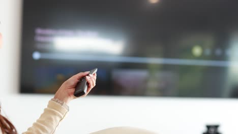 an asian woman uses a remote control to navigate a smart tv streaming menu in a bright, modern living room with soft natural lighting