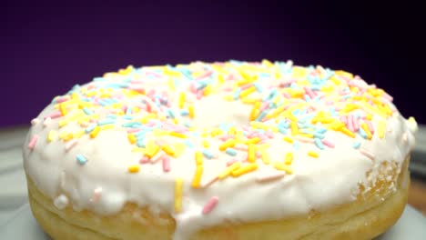 delicious sweet donut rotating on a plate. side view. bright and colorful sprinkled donut close-up macro shot spinning on a violet background.