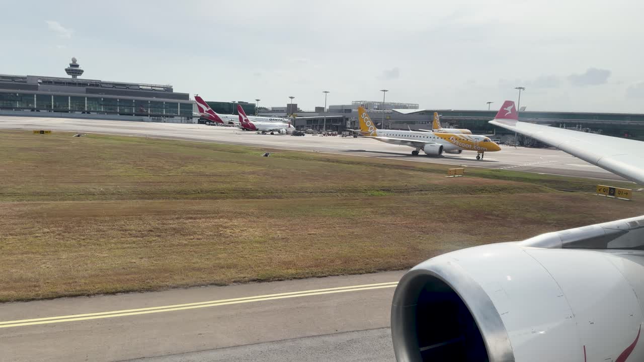 Vista dal finestrino di un passeggero mostra un motore a reazione e un'ala che rullano davanti ai terminal dell'aeroporto.