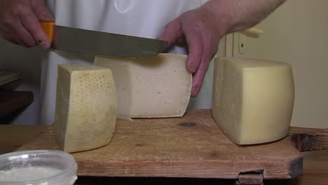 Käser-In-Weißer-Schürze-Schneidet-Stück-Lokalen-Käse-Mit-Riesigem-Messer,-Bietet-Dem-Kunden-An,-Statische-Nahaufnahme