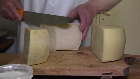 cheese maker in white apron cuts piece of local cheese with giant knife, offers in to customer, closeup static shot