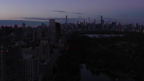 long drone flyover new york city's central park with harlem meer and onassis reservoir in view under the skyline at daybreak dawn sunrise blue hour