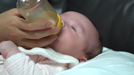 newborn infant baby girl drinking formula milk from the bottle at home close up and hands and plastic bottle and baby's head