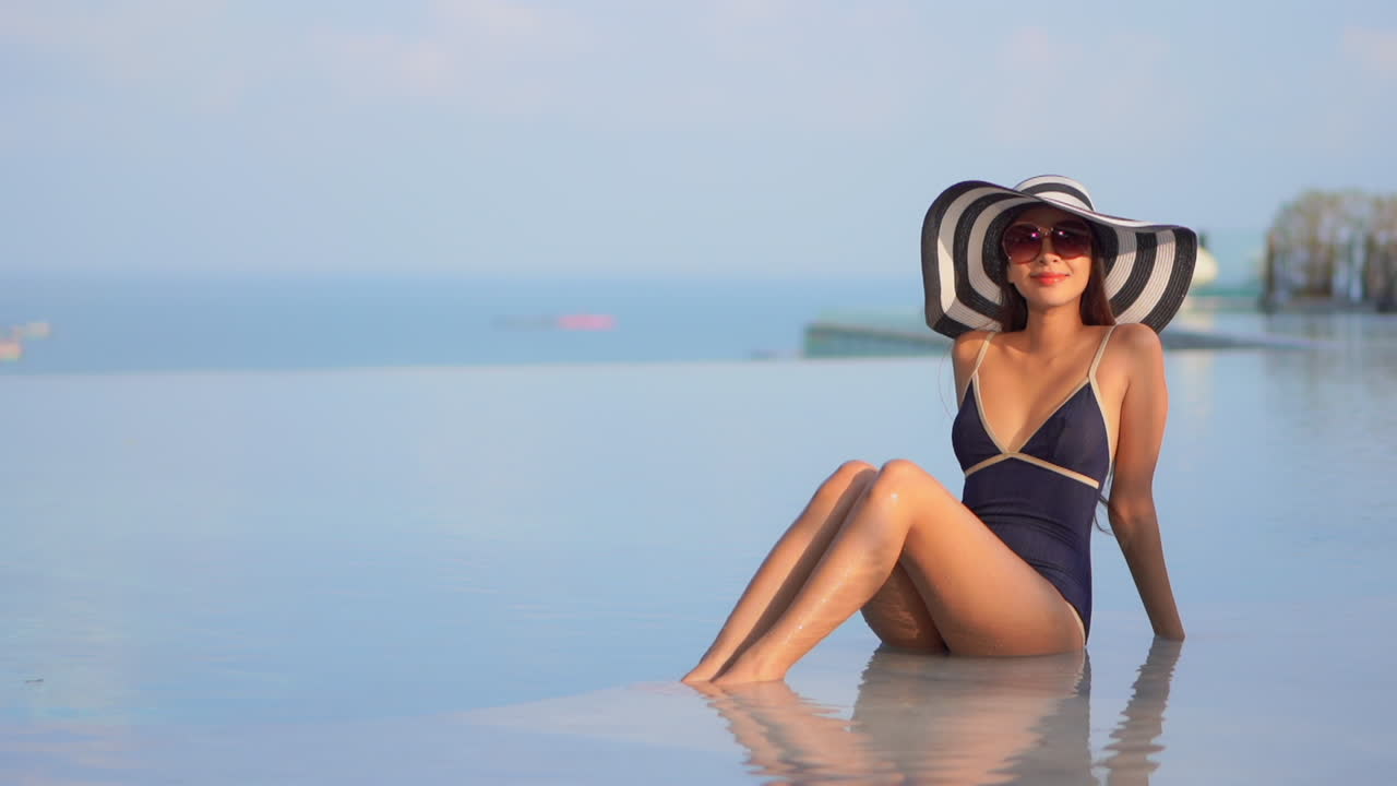Happy asian model posing at a pool in a swimsuit