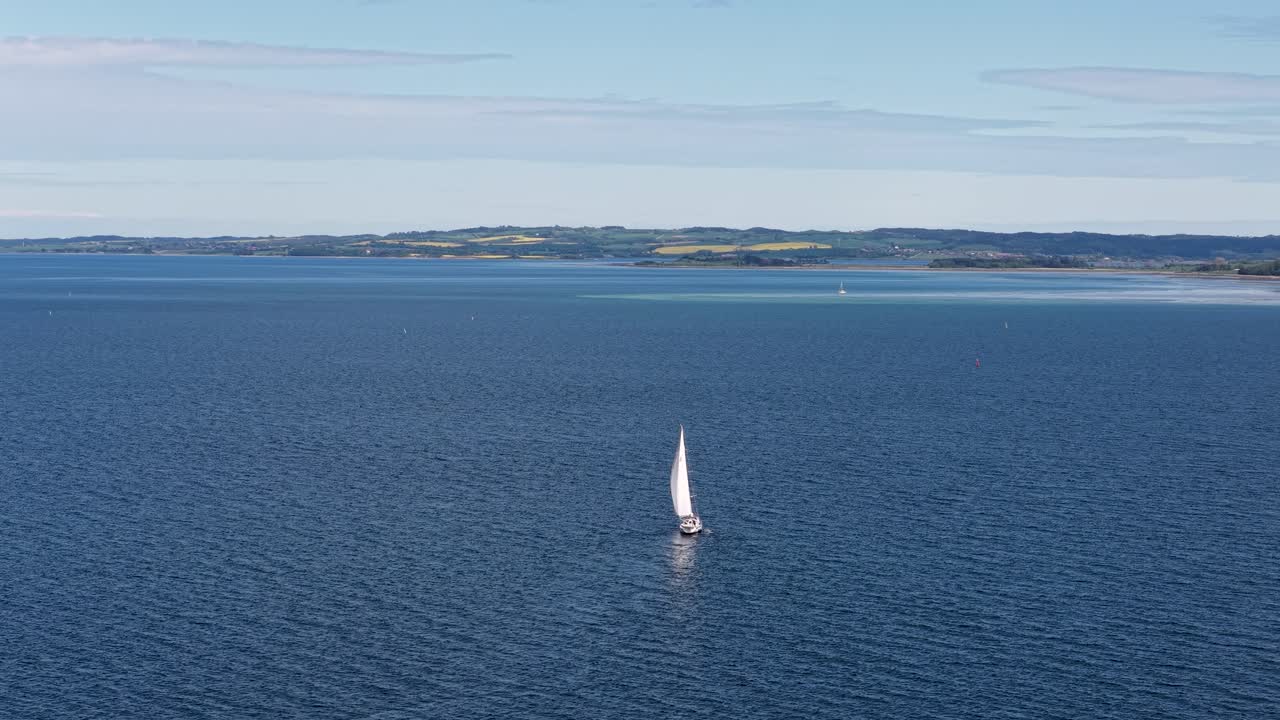 Aerial drone view of a sailboat gliding across calm blue waters near the shoreline of the Upper Peninsula of Michigan