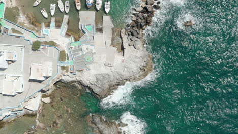 Aerial-Overhead-Top-Down-view-of-Greek-Fishing-Village-with-Waves-crashing-into-Rocks-on-Milos-Island