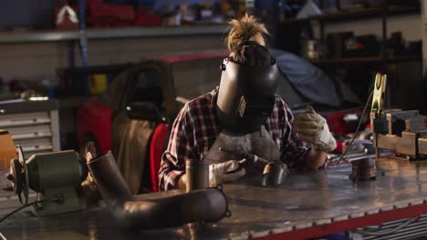 female mechanic wearing welding helmet welding while sitting at car service station