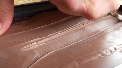 an artist in a studio carving brown modeling clay with a sharp hand tool in a satisfying shaving to start his art sculpture