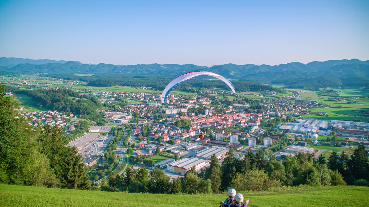 Paraglider pilot launch from a grass hill overseeing the city. Extreme sports