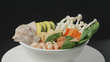 close up of a bowl of shabu ingredients spinning around on white table in the black background kitchen