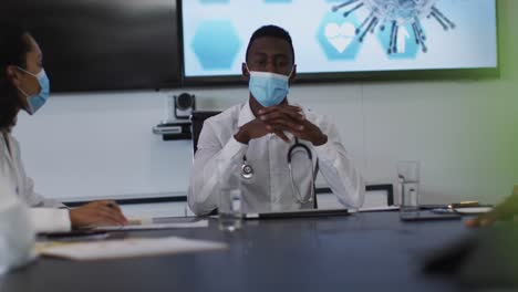 African-american-male-doctor-wearing-mask-giving-presentation-in-meeting-room