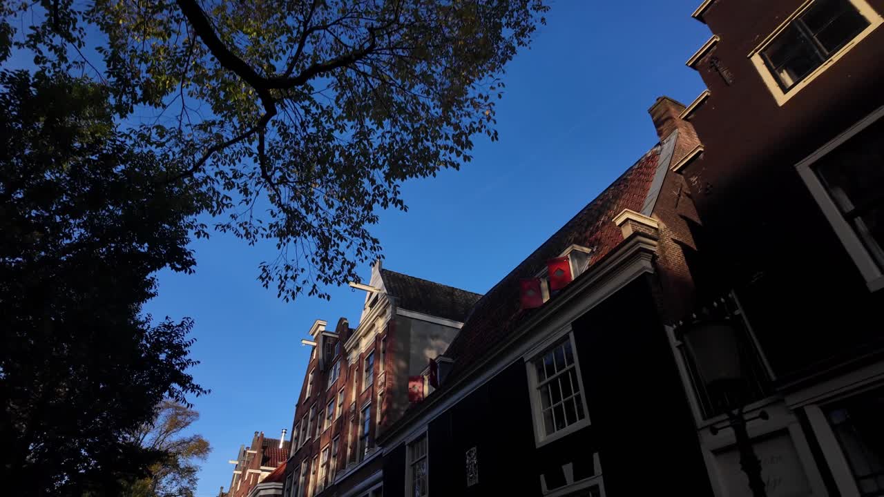 Visão de close-up em ângulo baixo de casas com frontões escalonados e arquitetura de tijolos sob um céu azul claro na histórica Amsterdã