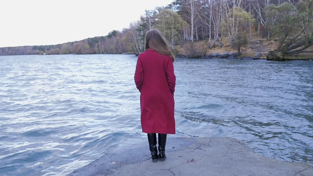 Nainen punaisessa takissa järven rannalla