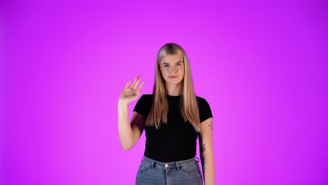 retrato de una mujer bonita y rubia agitando la mano en un gesto de saludo, toma de estudio con fondo púrpura