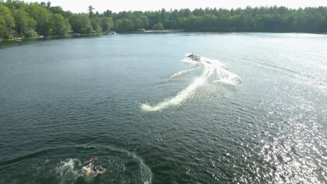 Speedboat-was-pulling-a-man-on-a-Skii-and-was-driving-him-on-a-blue-lake-that-was-surrounded-by-lush-green-trees-and-few-homes-around-mid-day