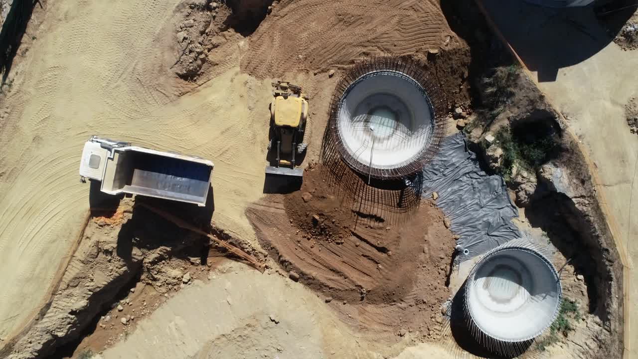 Truck dumps soil pile on commercial construction site, aerial view