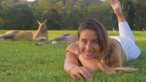 mujer alegre tumbada en la hierba verde junto con canguros grises orientales - costa dorada, qld, australia