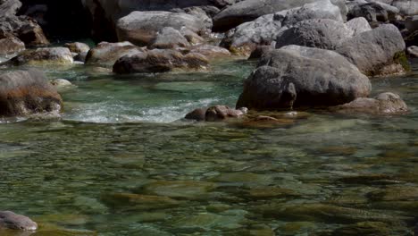 Steine-Des-Flussbetts,-Die-Von-Kristallklarem-Wasser-Des-Bergflusses-Gewaschen-Wurden,-Der-Aus-Geschmolzenem-Schnee-Strömt