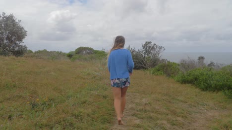 beautiful caucasian woman walking in bare feet on grassy hill by the sea coast