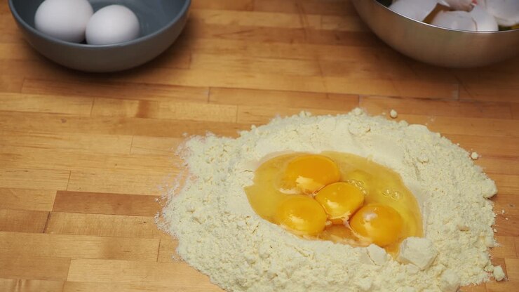 Fresh egg pasta dough preparation with a mound of flour and egg yolks over a wooden table - High angle medium shot
