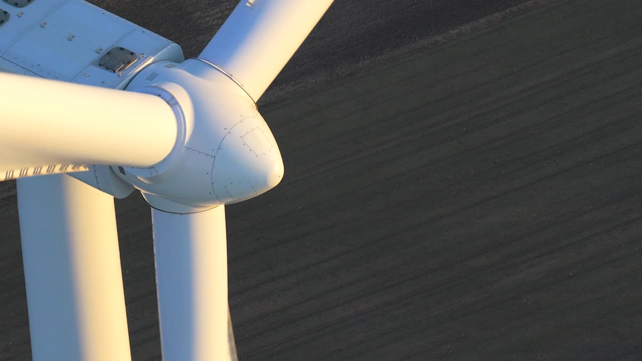 Close up aerial shot of wind turbine blades rotating. Golden hour sunlight illuminates the massive infrastructure, creating clean, renewable energy