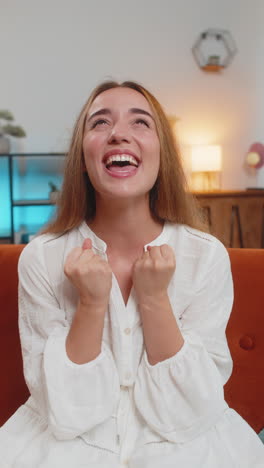 happy young woman watching tv celebrating success winning lottery luck victory sitting on couch