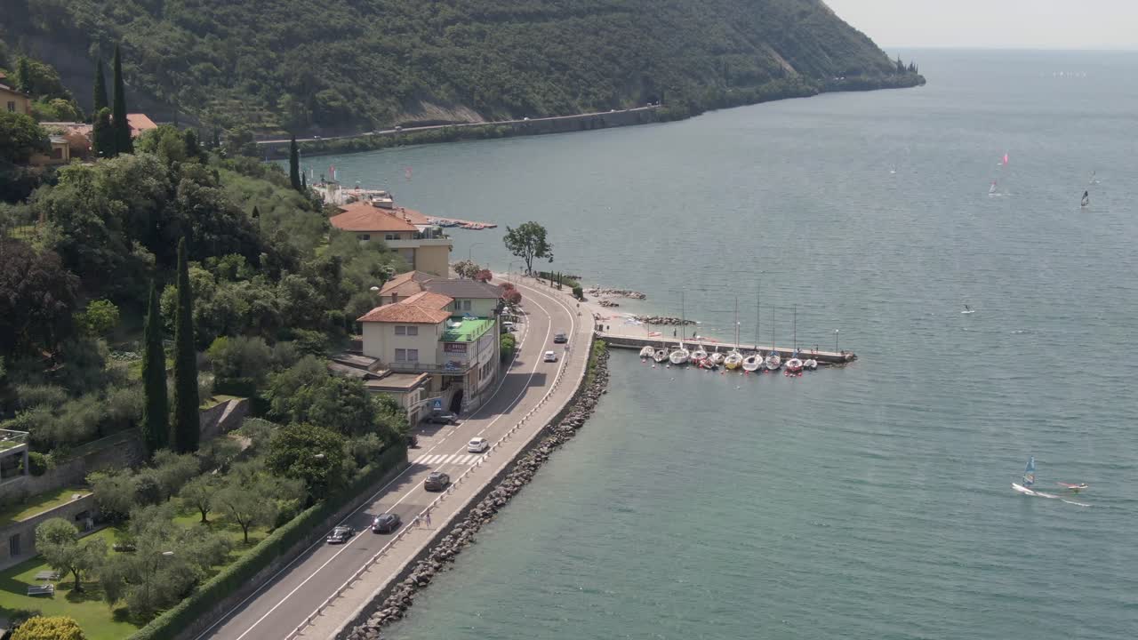 Vista aerea del lungolago sul Lago di Garda con auto sulla strada e windsurfisti sul lago in una giornata di sole