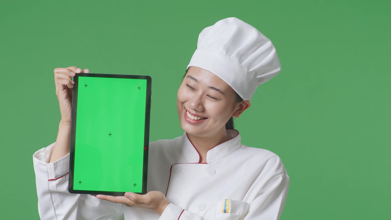 Close Up Of Asian Woman Chef Smiling And Showing Green Screen Tablet To The Camera While Standing In The Green Screen Background Studio